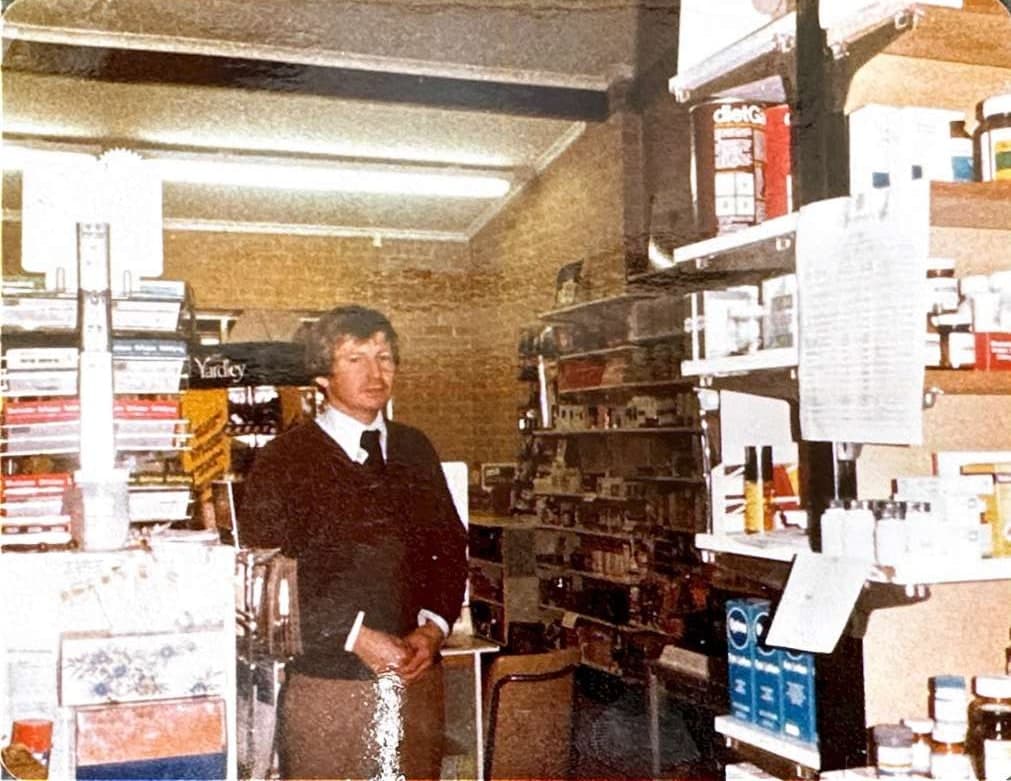 Keith Chapman standing behind the dispensary counter at Byford Pharmacy in its early years.
